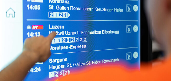 Blick über die Schulter auf das Smart Information Display mit den Abfahrtszeiten der nächsten Züge.