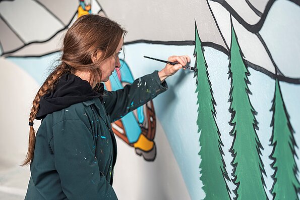 Corinne Weidmann malt Tannen auf die Wand der Unterführung